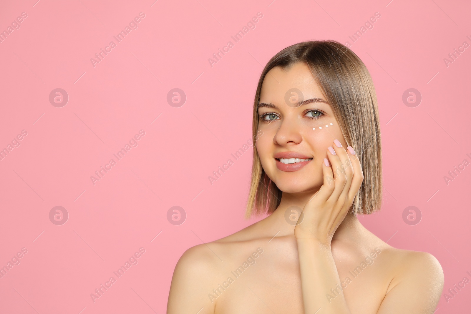 Photo of Young woman with cream around eye on pink background, space for text