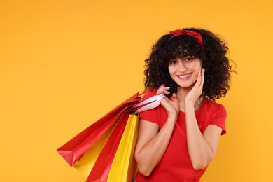 Happy young woman with shopping bags on yellow background