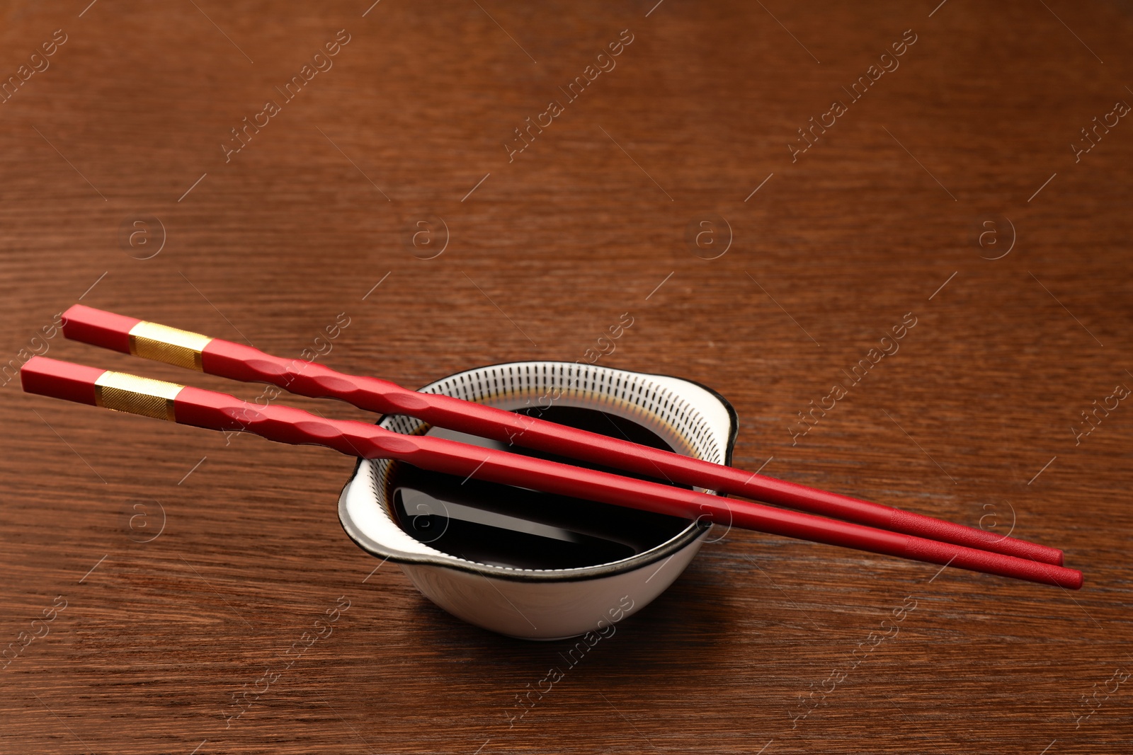 Photo of Bowl with soy sauce and chopsticks on wooden table