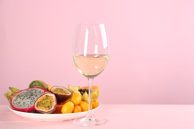 Delicious exotic fruits and wine on pink wooden table. Space for text