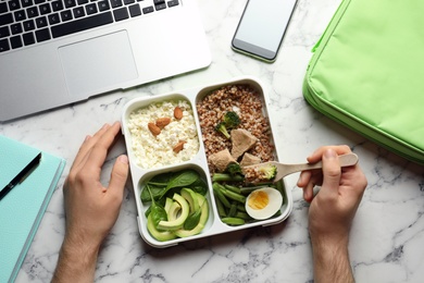 Photo of Man eating natural protein food from container at office table, top view