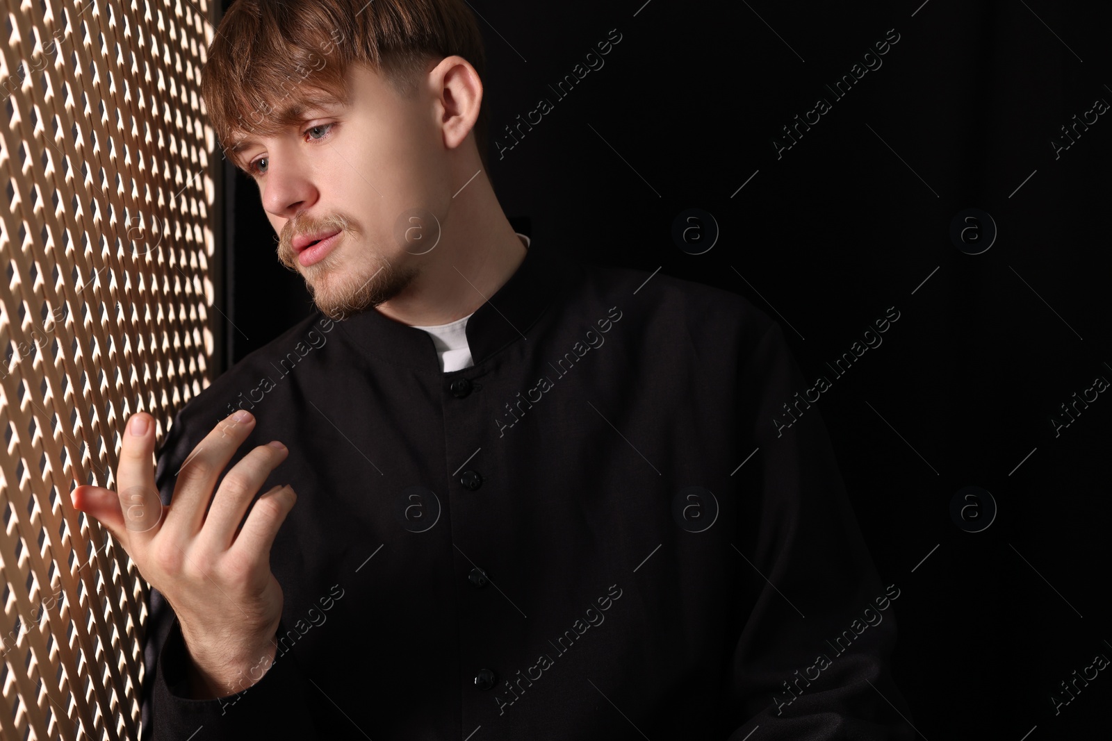 Photo of Catholic priest talking to parishioner in confessional booth