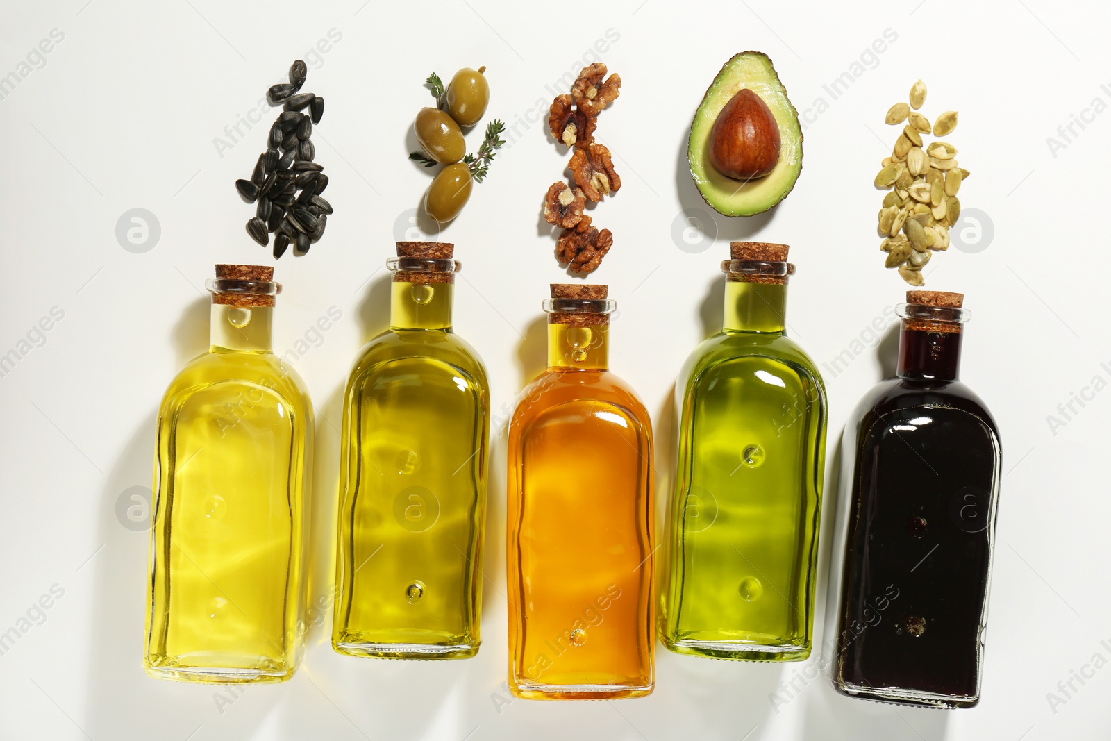 Photo of Vegetable fats. Different cooking oils in glass bottles and ingredients on white background, flat lay