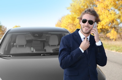 Photo of Young businessman talking on phone near modern car, outdoors