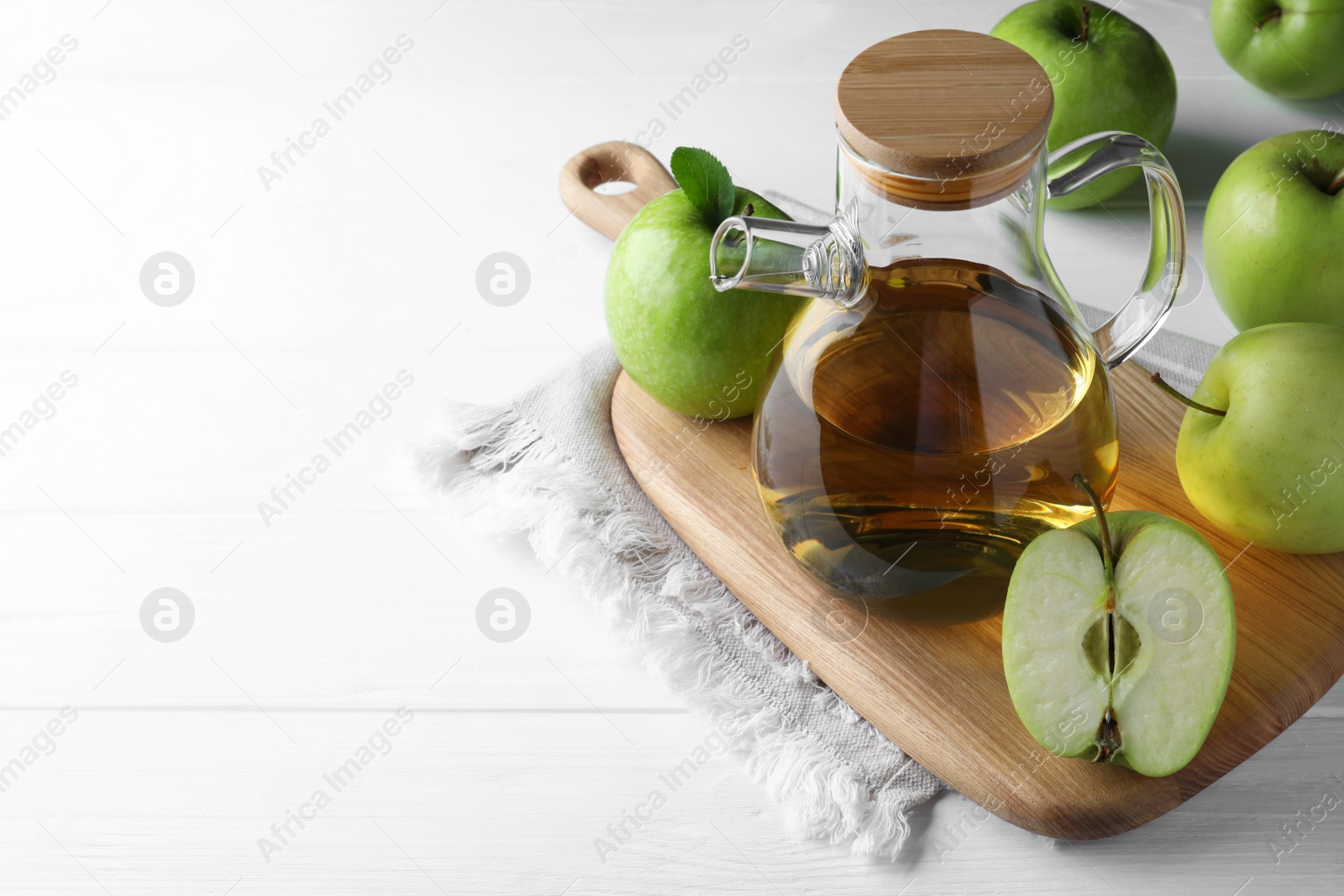 Photo of Jug of tasty juice and fresh ripe green apples on white wooden table, space for text