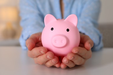 Woman with pink piggy bank at white table, closeup