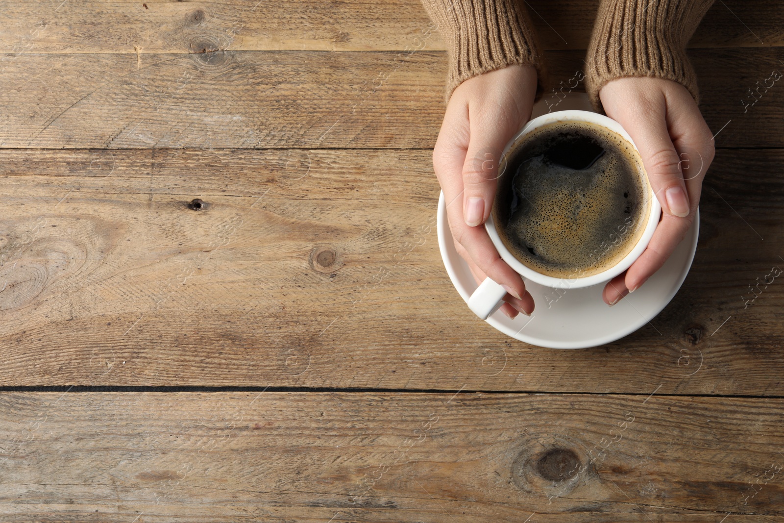 Photo of Woman with cup of hot aromatic coffee at wooden table, top view. Space for text