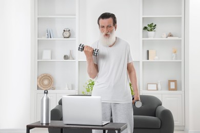 Photo of Senior man exercising with dumbbells while watching online tutorial at home. Sports equipment