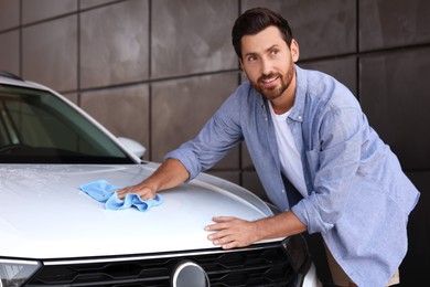 Photo of Handsome man cleaning car hood with rag outdoors