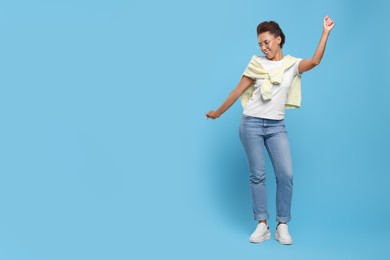 Photo of Happy young woman in eyeglasses dancing on light blue background. Space for text
