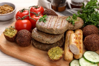 Different tasty vegan meat products and fresh vegetables on wooden table, closeup