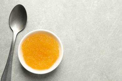 Fresh pike caviar in bowl and spoon on light grey table, top view. Space for text