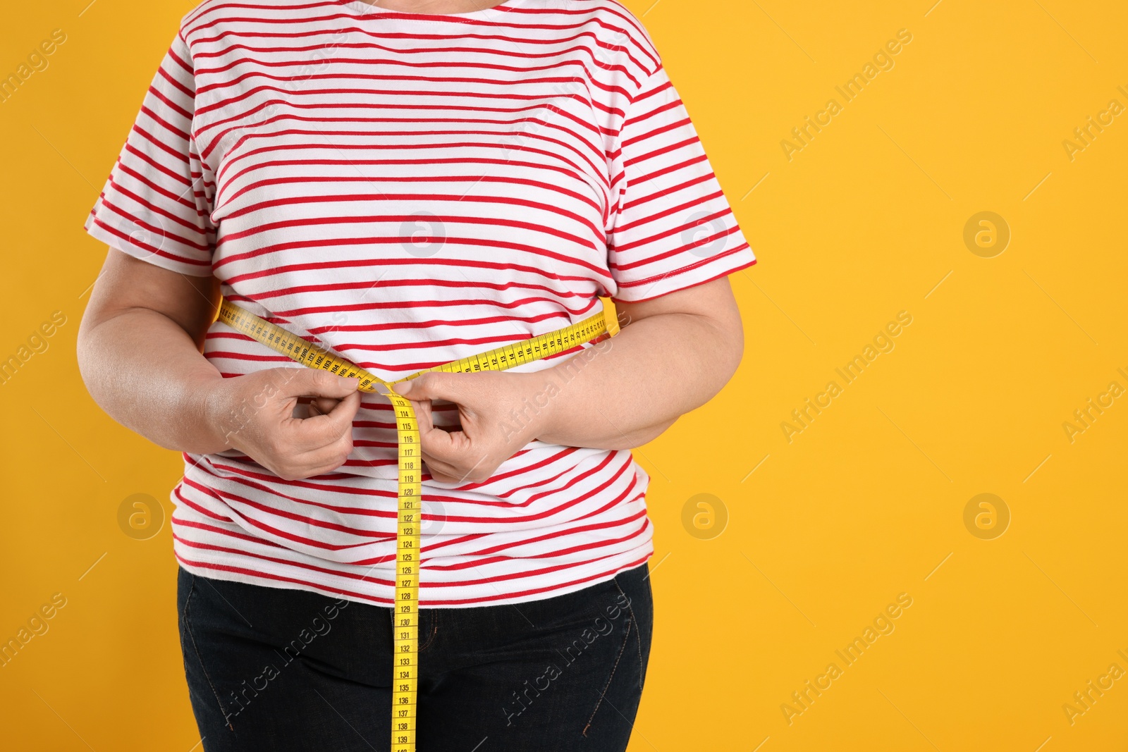 Photo of Overweight woman measuring waist with tape on orange background, closeup