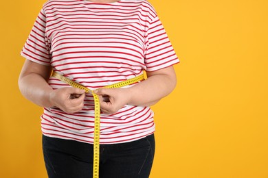 Overweight woman measuring waist with tape on orange background, closeup