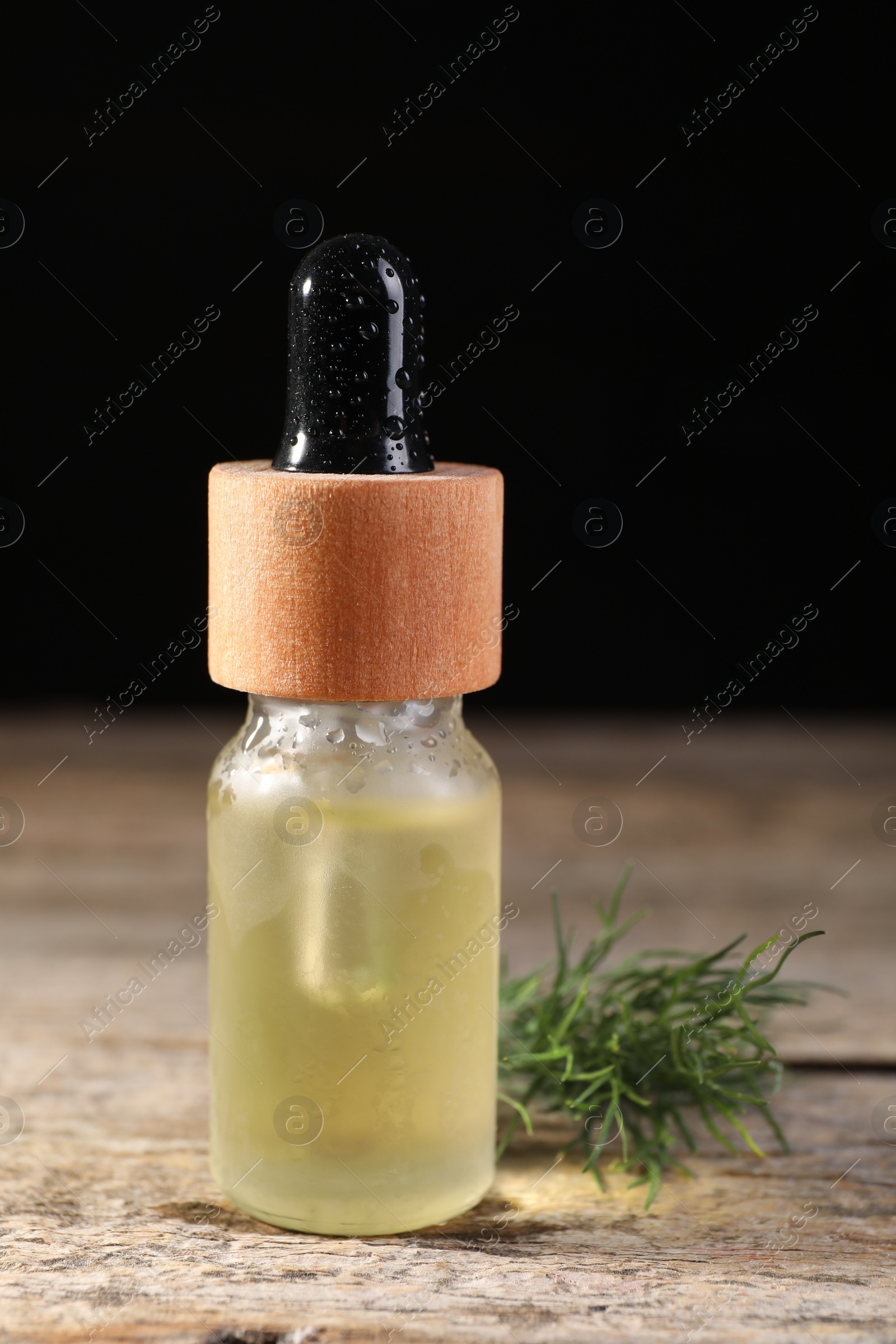 Photo of Bottle of essential oil and fresh dill on wooden table