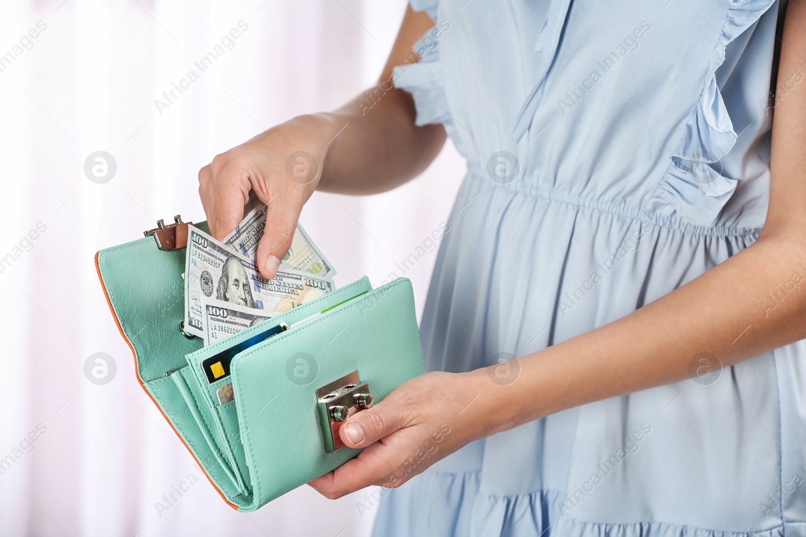 Photo of Woman taking out cash from stylish wallet on light background, closeup