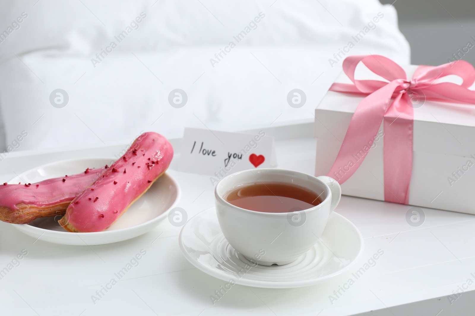 Photo of Tasty breakfast served in bed. Delicious eclairs, tea, gift box and I Love You card on tray