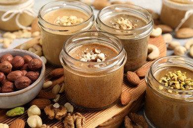 Photo of Tasty nut butters in jars and raw nuts on table, closeup