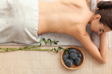 Beautiful young woman relaxing after massage on bamboo mat, top view