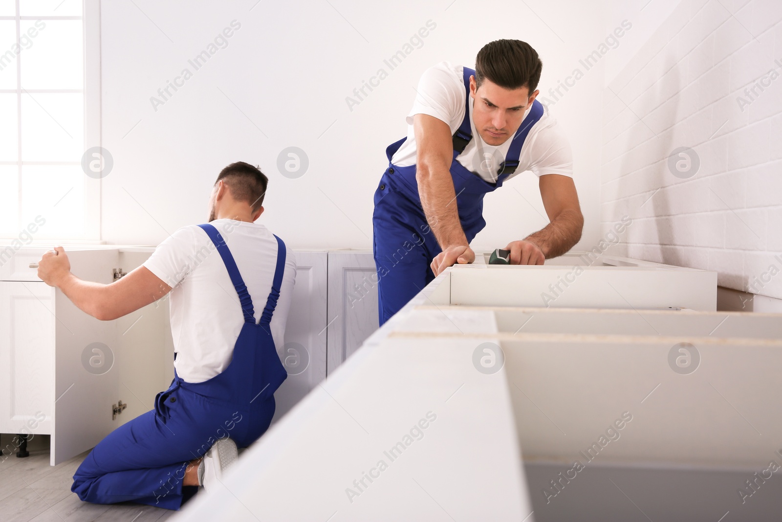 Photo of Maintenance workers installing new kitchen furniture indoors