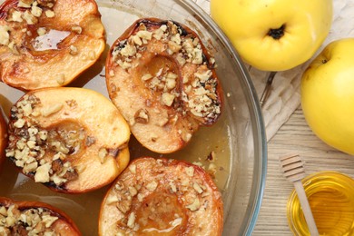Delicious baked quinces with nuts in bowl, honey and fresh fruits on wooden table, flat lay