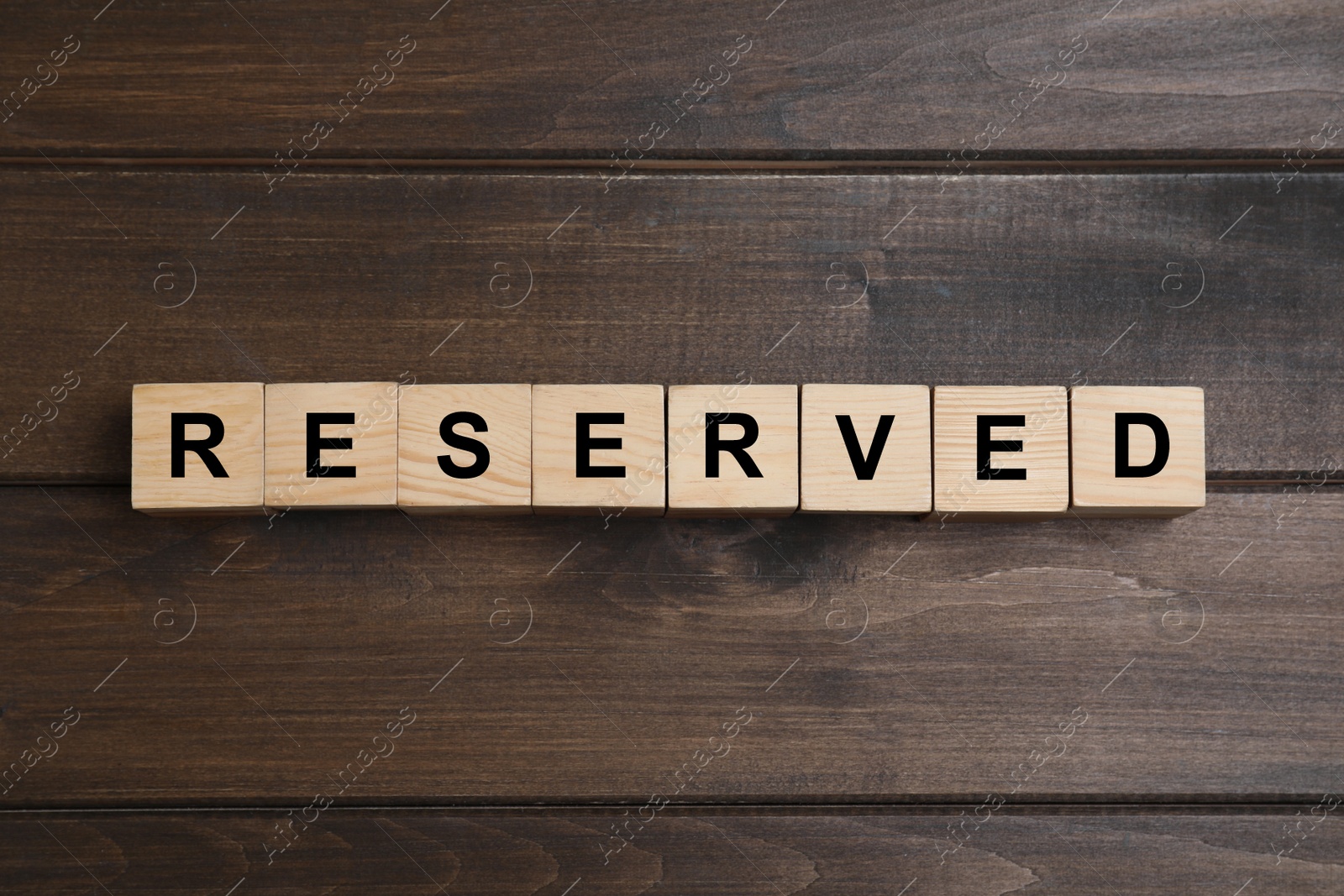 Photo of Word RESERVED made with cubes on wooden surface, top view. Table setting element