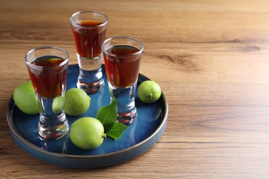 Photo of Delicious liqueur and green walnuts on wooden table. Space for text