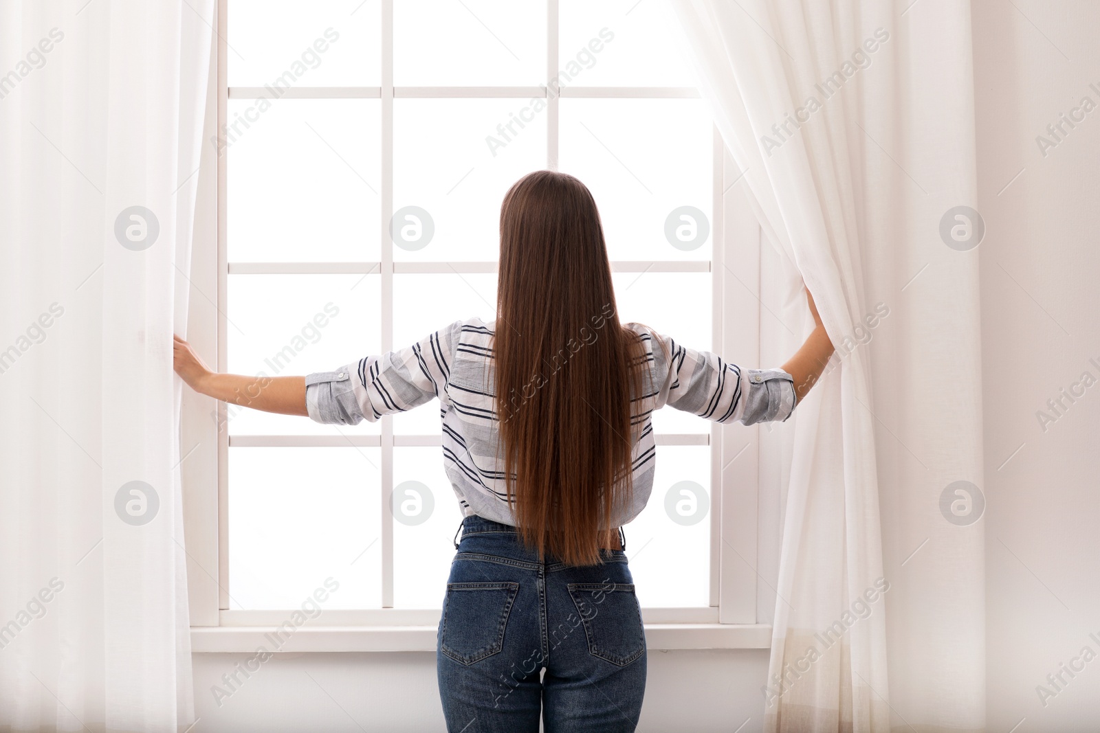 Photo of Young woman opening window curtains at home