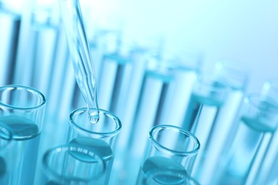 Dripping liquid from pipette into test tube on light blue background, closeup