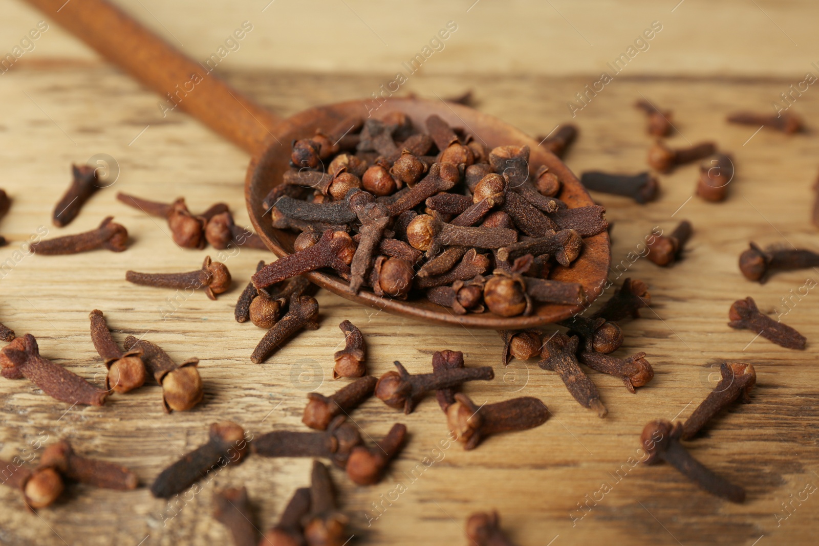 Photo of Aromatic dry cloves and spoon on wooden table, closeup