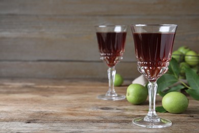 Photo of Delicious liqueur and green walnuts on wooden table. Space for text