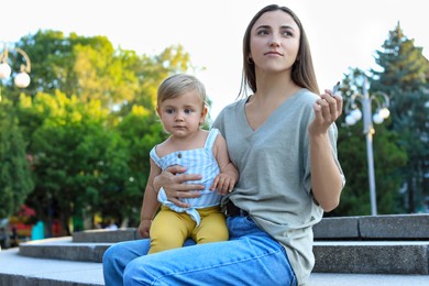 Photo of Mother with cigarette and child outdoors. Don't smoke near kids