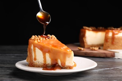 Pouring caramel sauce onto delicious piece of cheesecake with walnuts on black table, space for text