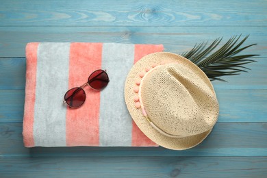 Beach towel, straw hat and sunglasses on light blue wooden background, flat lay