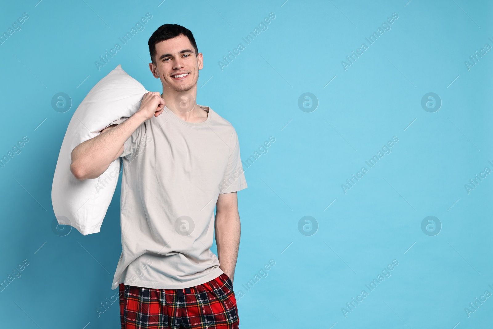 Photo of Happy man in pyjama holding pillow on light blue background, space for text