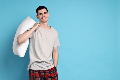 Photo of Happy man in pyjama holding pillow on light blue background, space for text