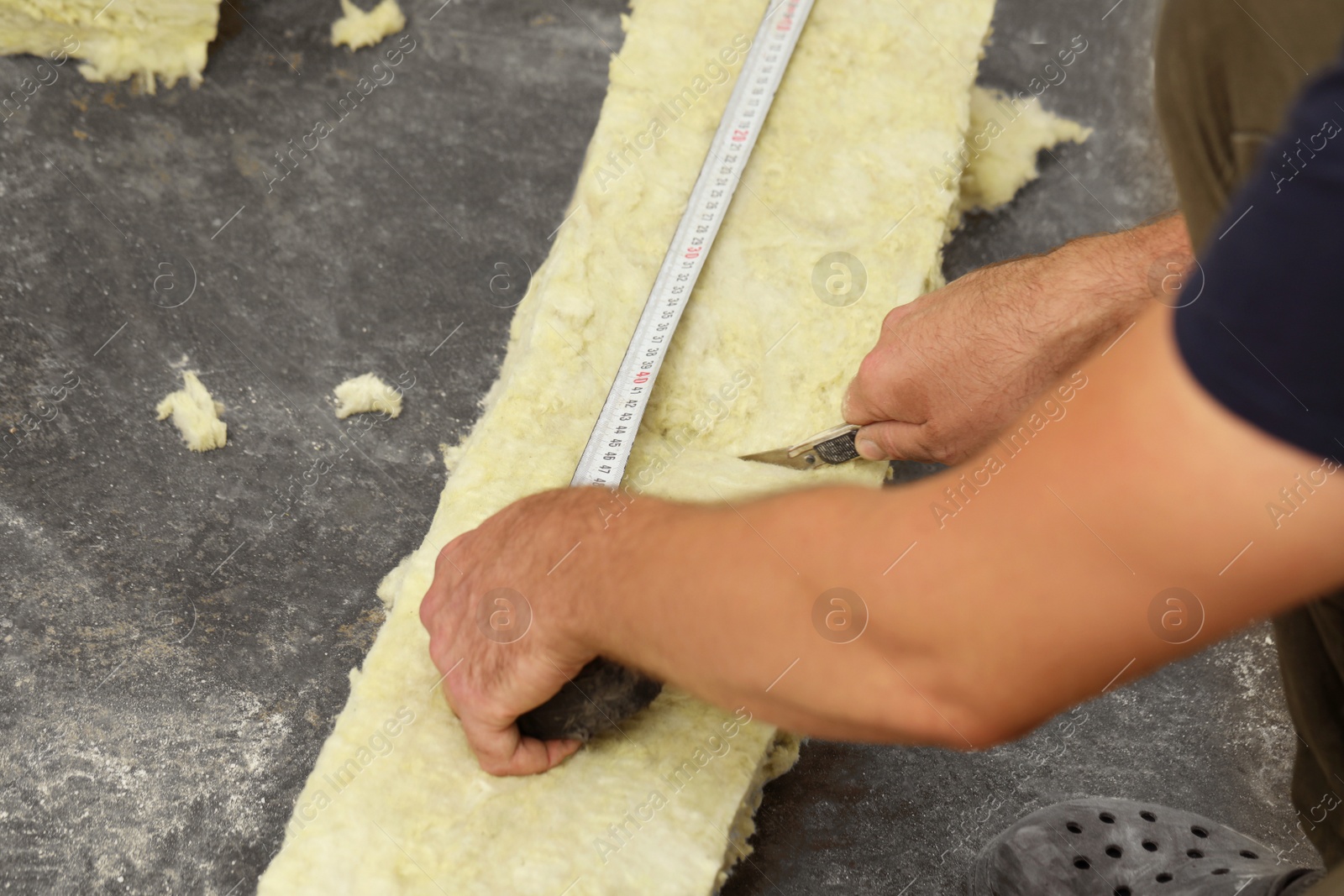 Photo of Worker measuring and cutting insulation material indoors, closeup