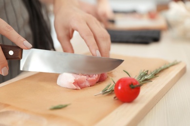 Photo of Female chef cutting meat on wooden board at table, closeup