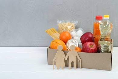 Photo of Humanitarian aid for elderly people. Different donation food products and figures of senior couple on white wooden table. Space for text