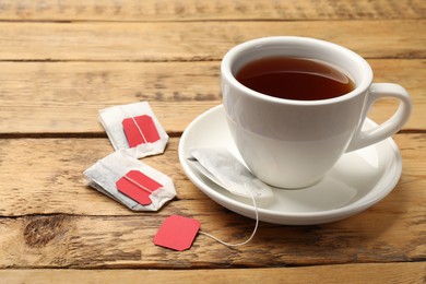 Photo of Tea bags and cup of hot beverage on wooden table, closeup. Space for text