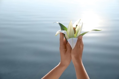 Photo of Woman with beautiful lily flower near river, closeup. Nature healing power