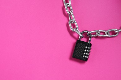 Photo of Steel combination padlock and chain on pink background, top view. Space for text