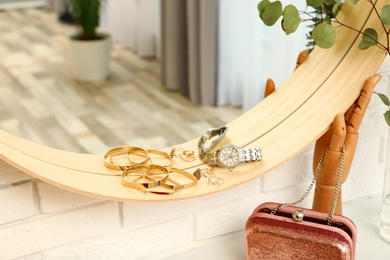 Photo of Round mirror with female accessories on brick wall indoors, closeup. Interior design