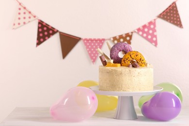 Delicious cake decorated with sweets and balloons on white wooden table, space for text