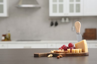 Photo of Wooden bord with cut cheese and, nuts and grape on countertop in kitchen, space for text