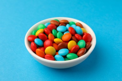 Photo of Bowl with tasty colorful candies on blue background, closeup