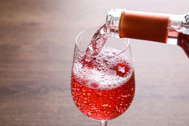Pouring delicious rose wine into glass on wooden table, closeup