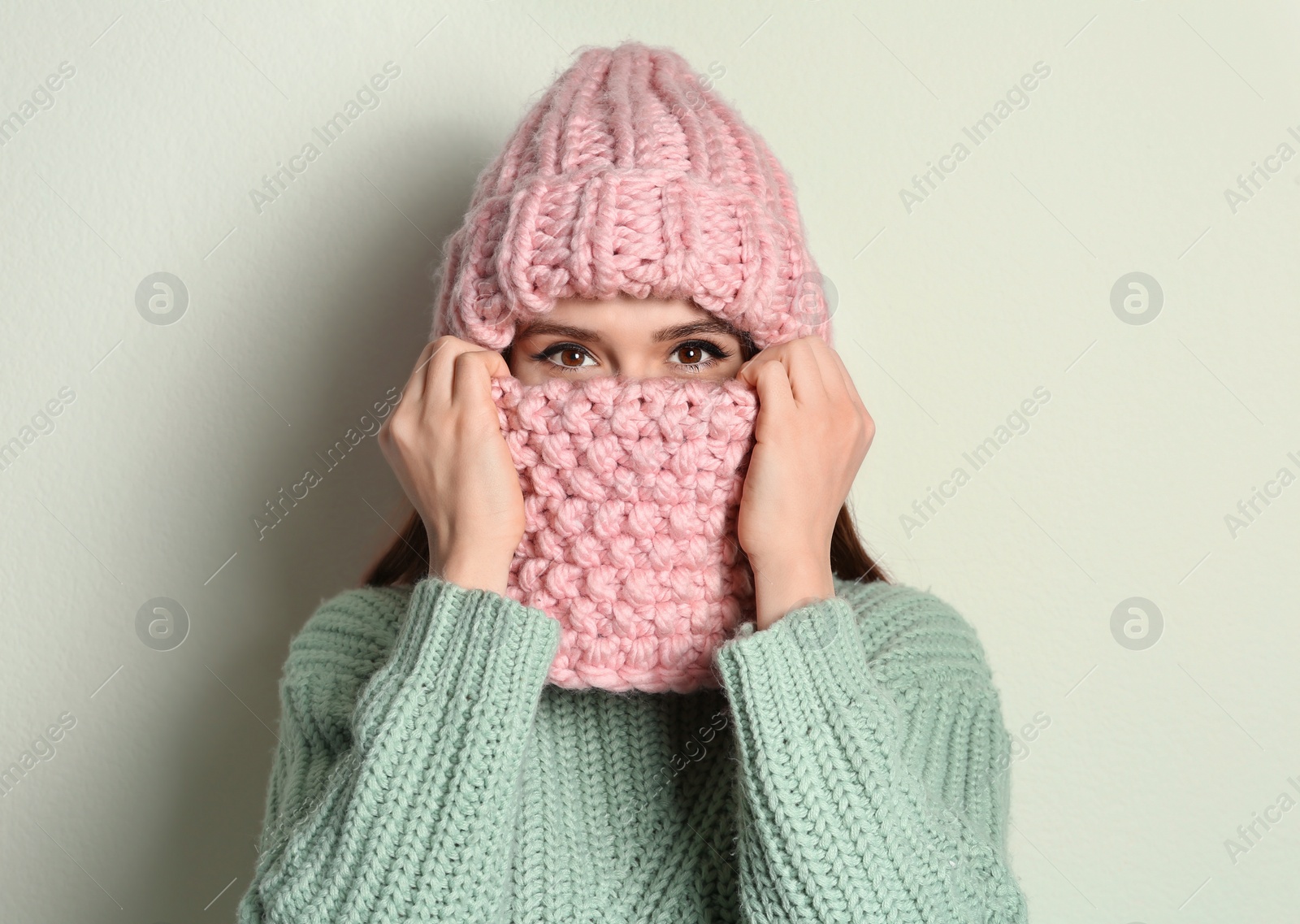 Photo of Young woman wearing warm sweater, snood and hat on light background. Winter season