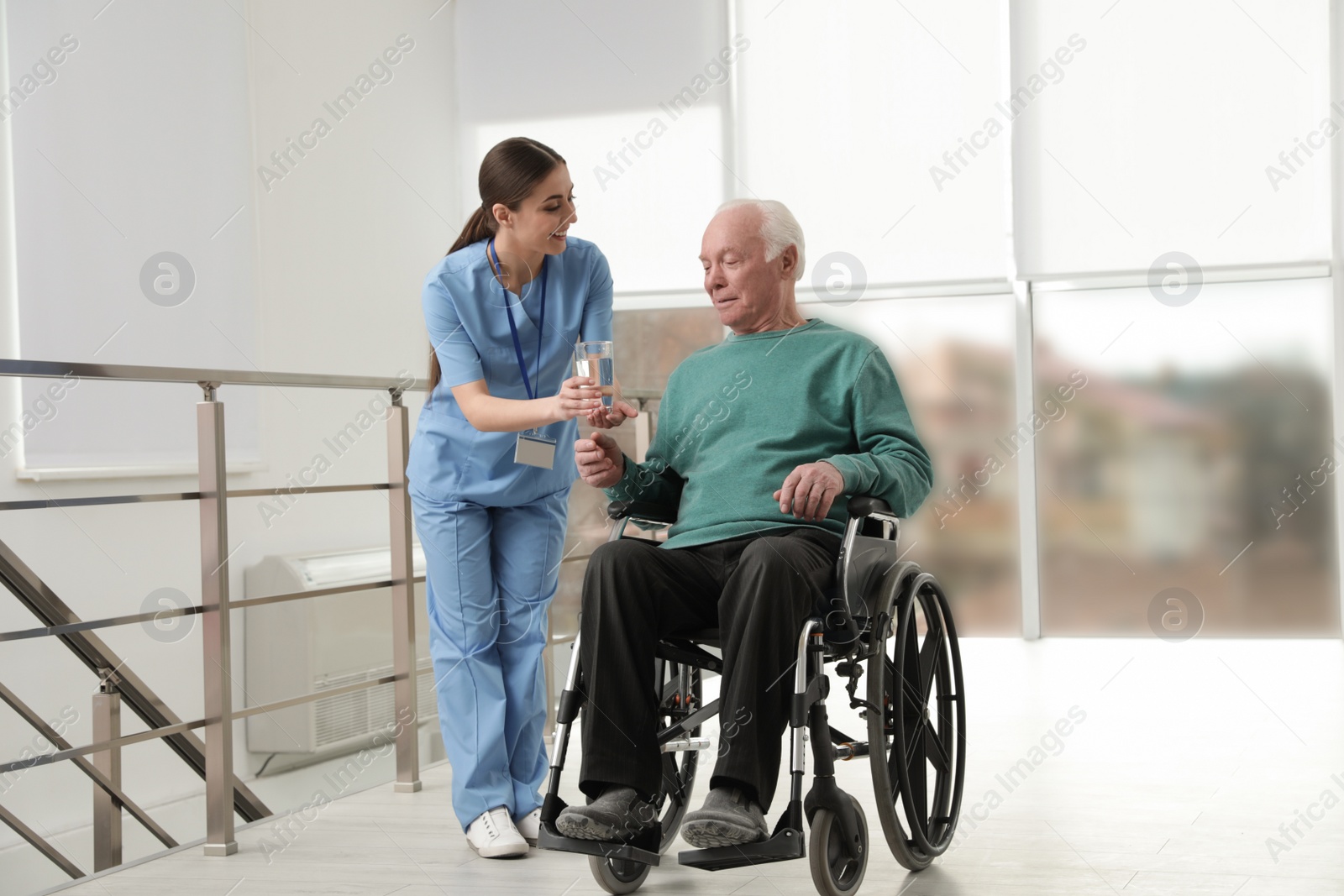 Photo of Nurse giving water to senior man in wheelchair at hospital. Medical assisting