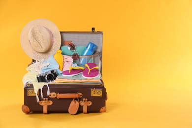 Photo of Packed vintage suitcase with different beach objects on orange background, space for text. Summer vacation